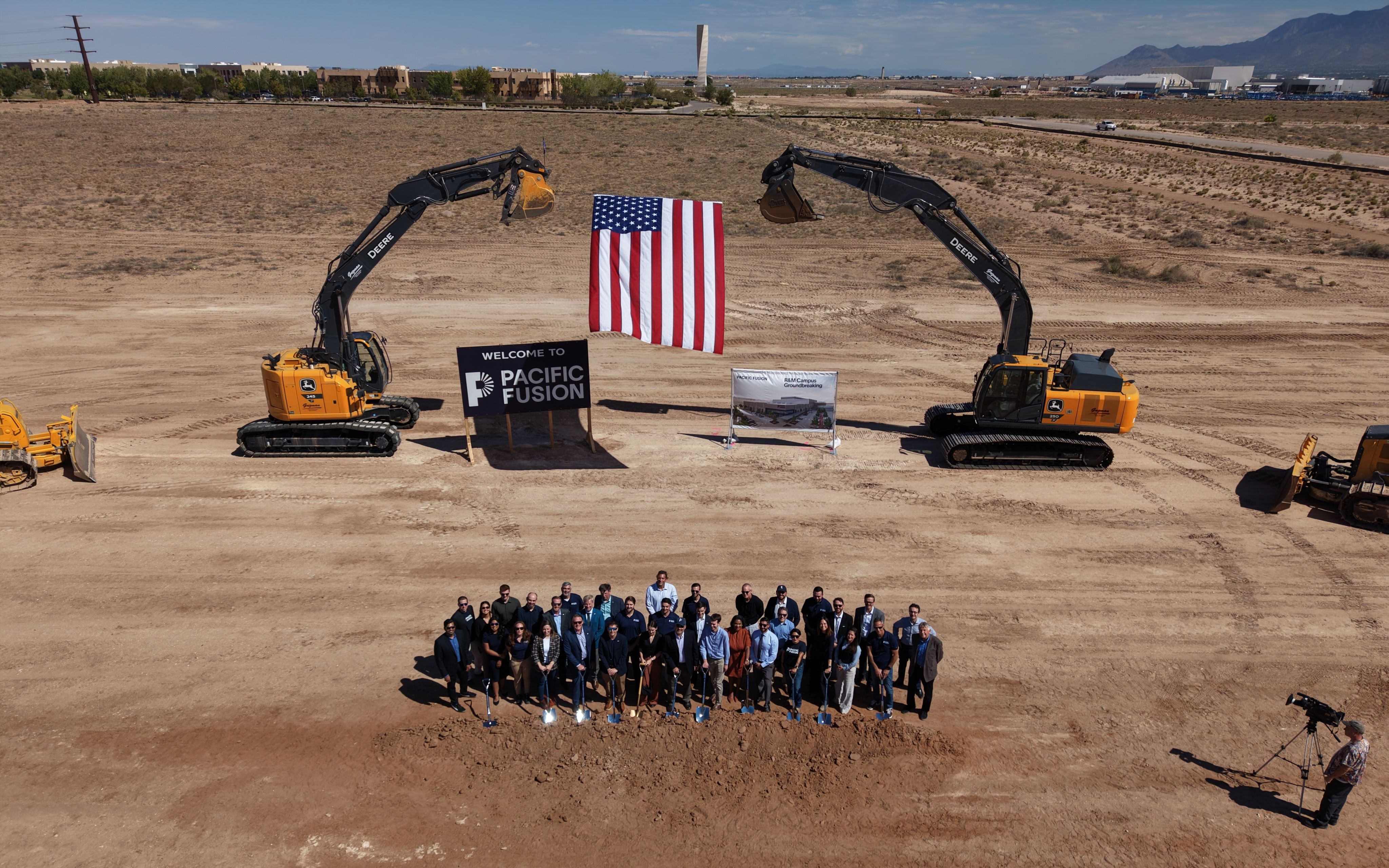 Attendees with ceremonial shovels at Pacific Fusion’s Albuquerque groundbreaking, beneath an American flag suspended between excavators
