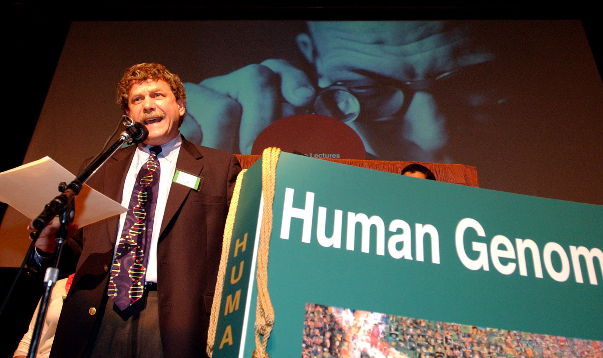 Eric Lander speaking beside a large Human Genome book prop at the 2003 Ig Nobel awards