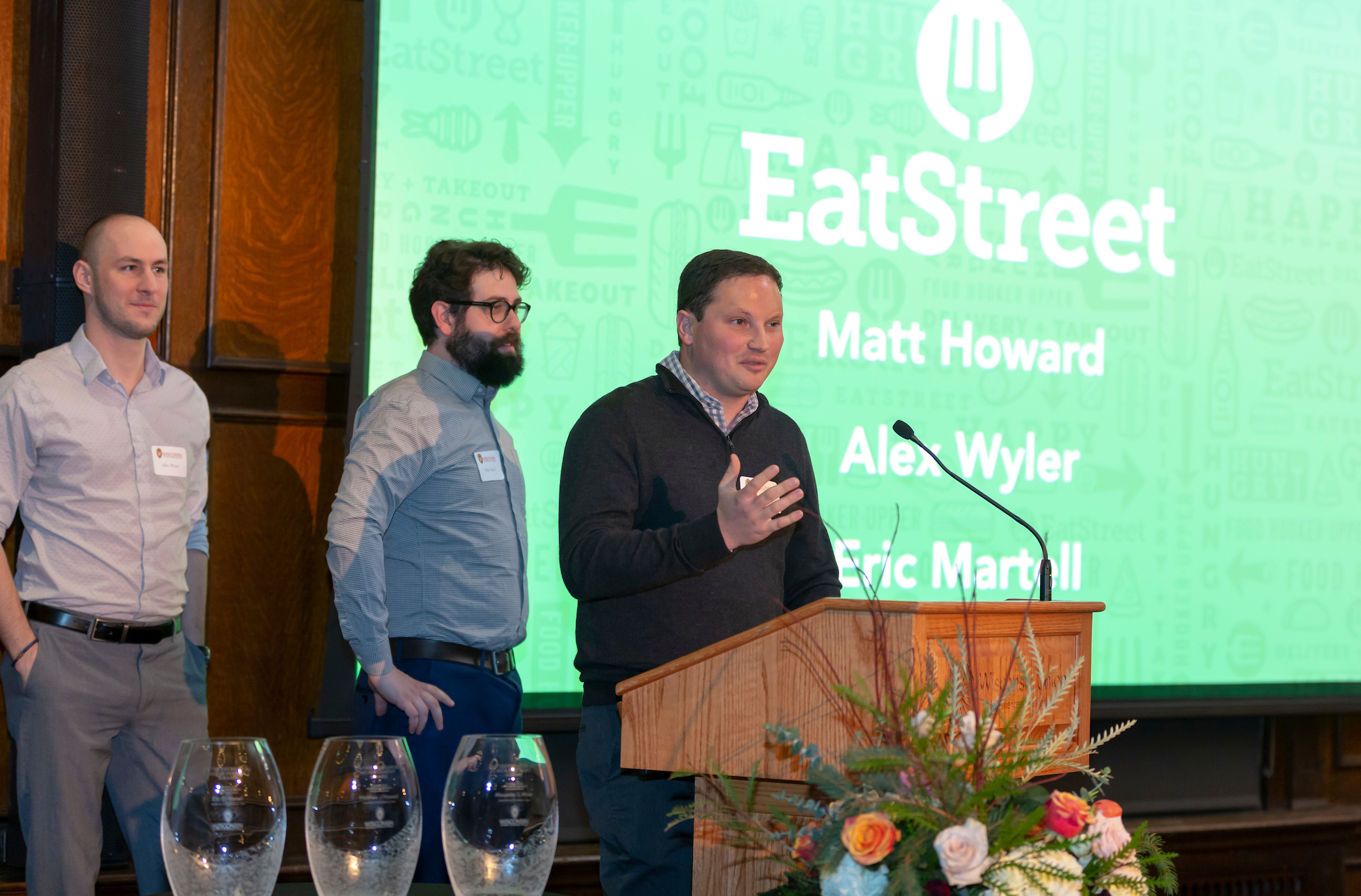 Alex Wyler and Eric Martell stand beside Matt Howard as he speaks at the 2018 UW-Madison entrepreneurial awards.
