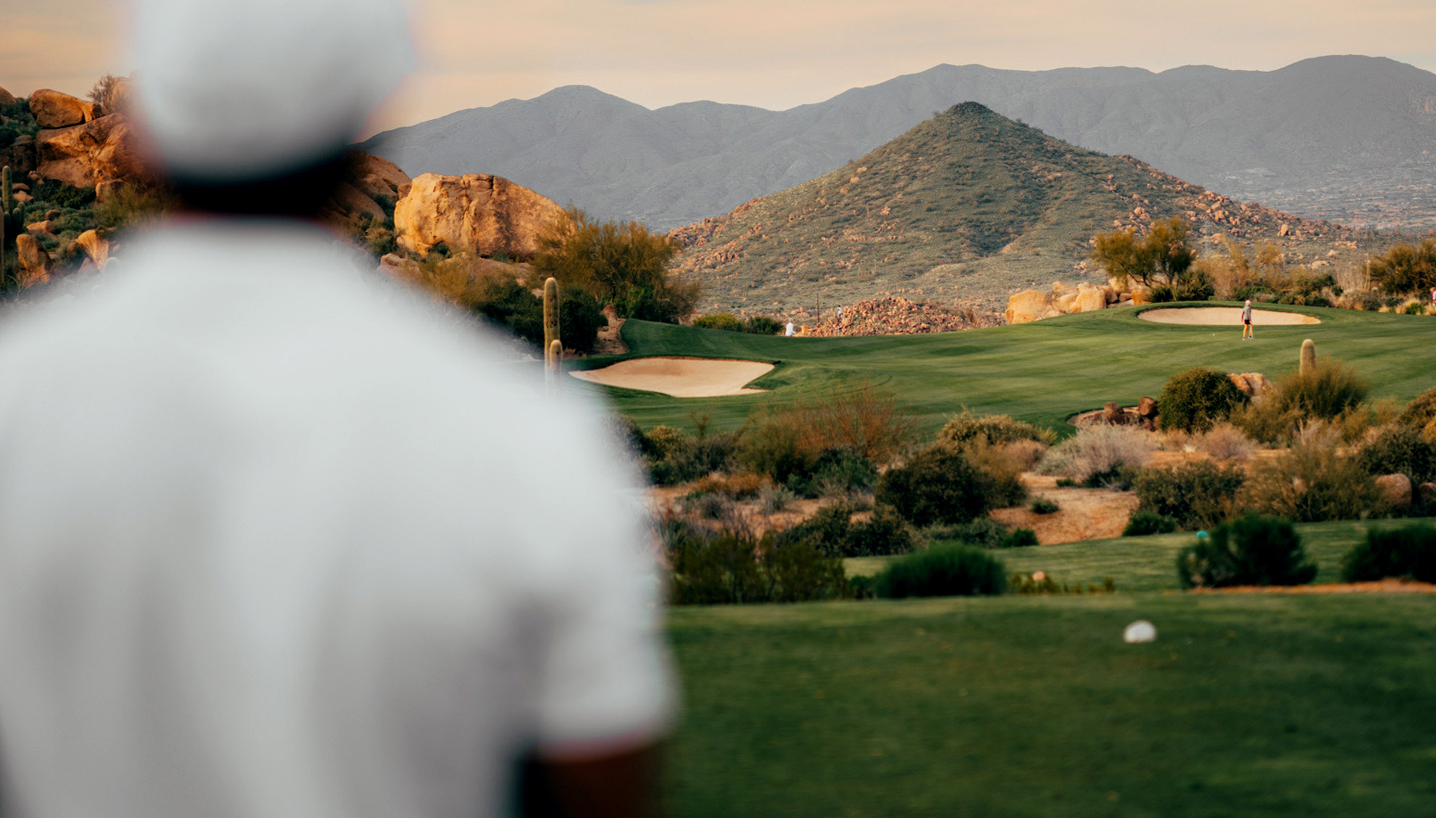 A golfer looking across a course framed by rocky hills and desert vegetation