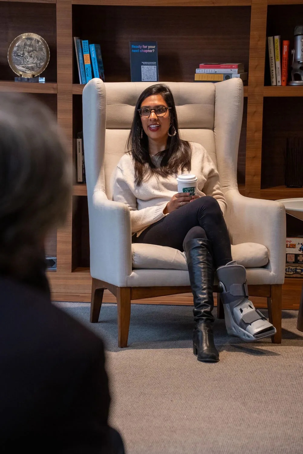 Erica Jain seated in an armchair with a takeaway coffee during a conversation