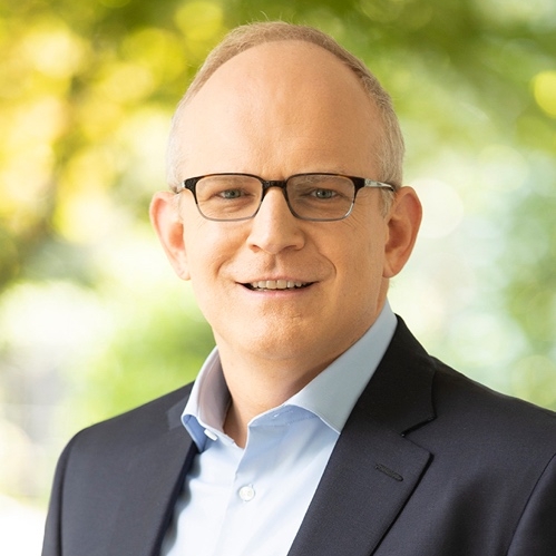 Press portrait of Erick Goss in a dark jacket and glasses