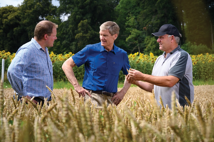 Erik Fyrwald, in a blue shirt, talking with two growers in a crop field