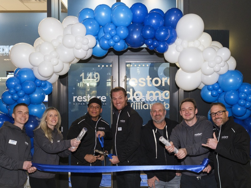 Erik Geisler and the Restore Hyper Wellness Williamsburg team at a ribbon cutting beneath blue and white balloons
