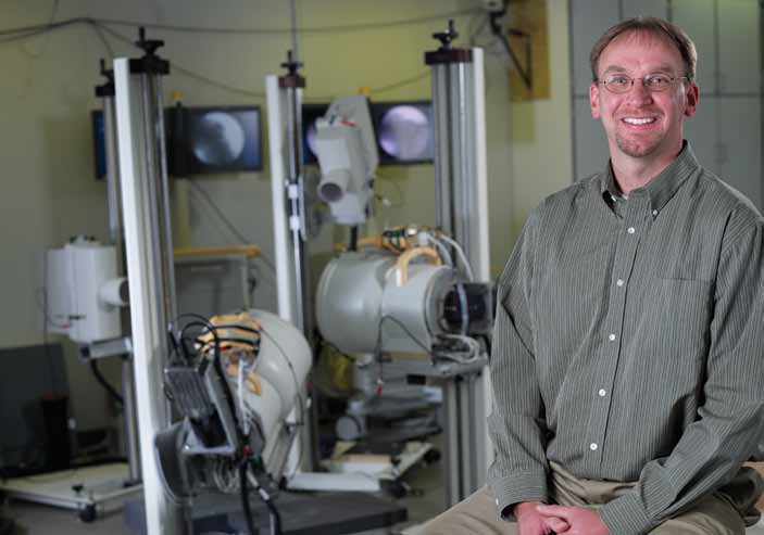 Erik Giphart seated beside biplane fluoroscopy equipment in a biomechanics laboratory