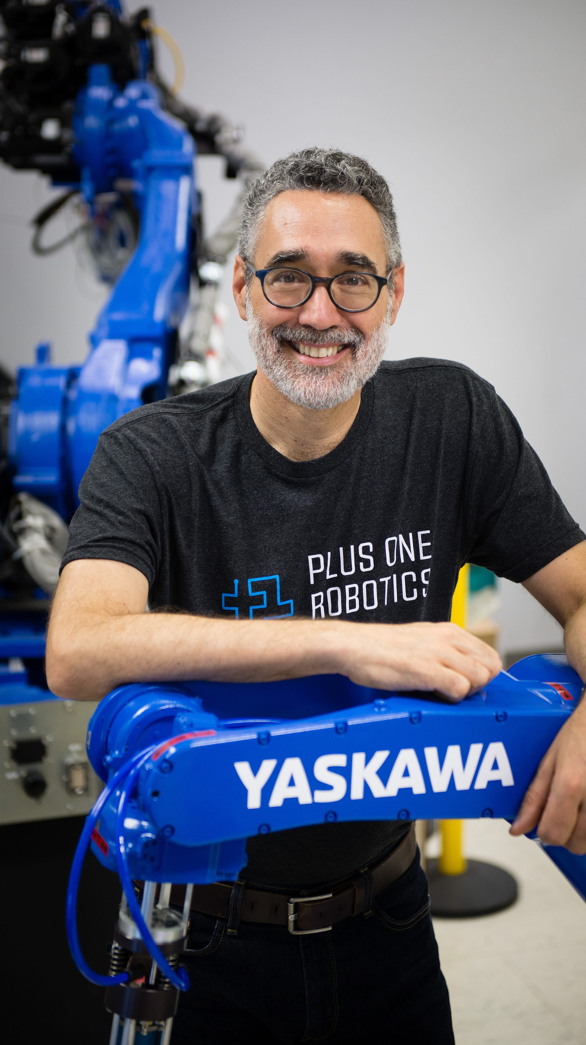 Erik Nieves leaning on a blue Yaskawa industrial robot in a workshop