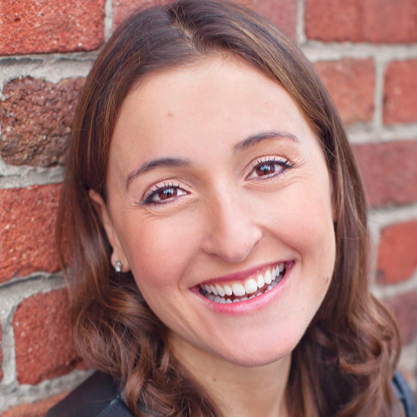 Erika White smiling in a portrait against a red brick wall