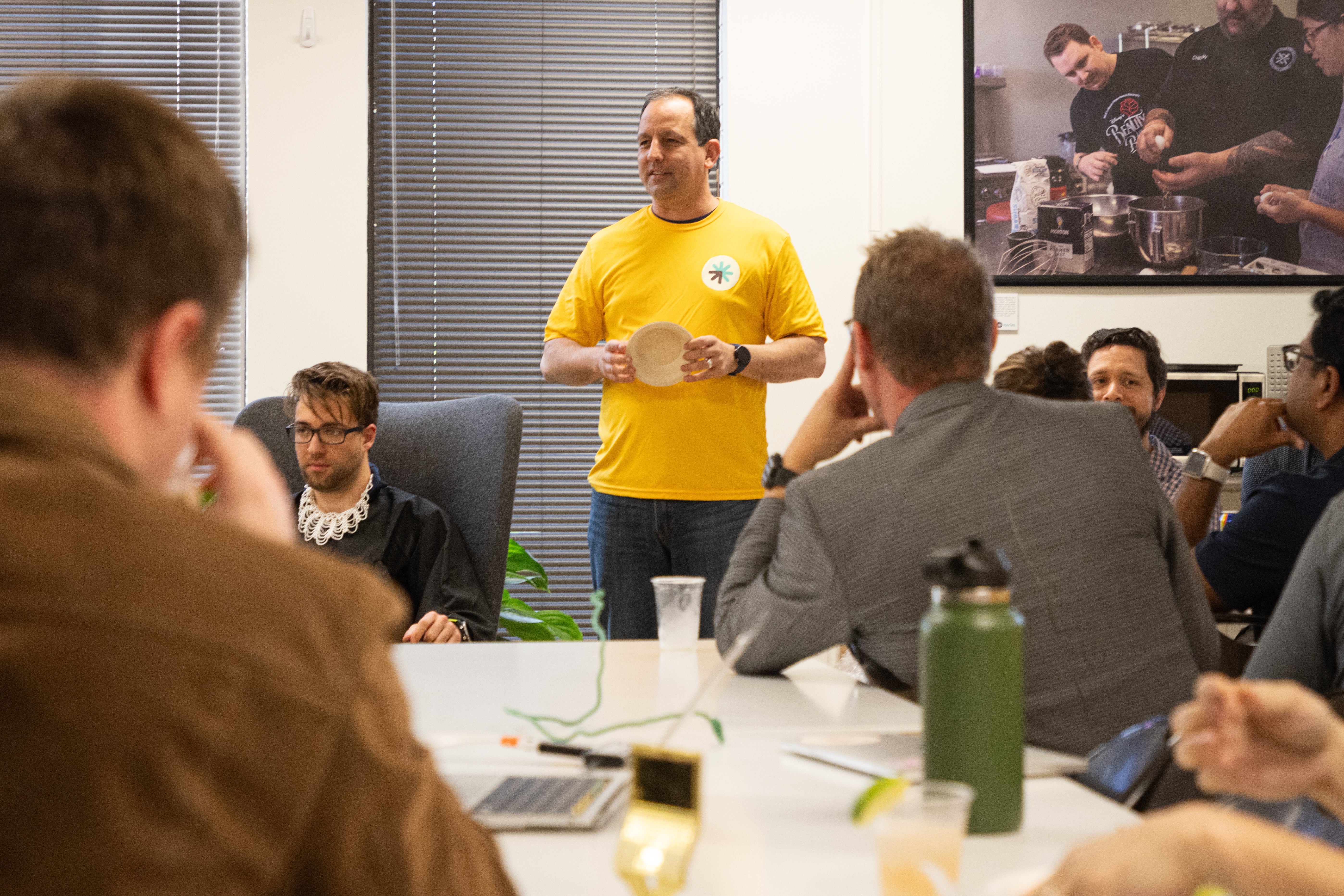 Erine Gray in a yellow shirt addressing a seated group indoors
