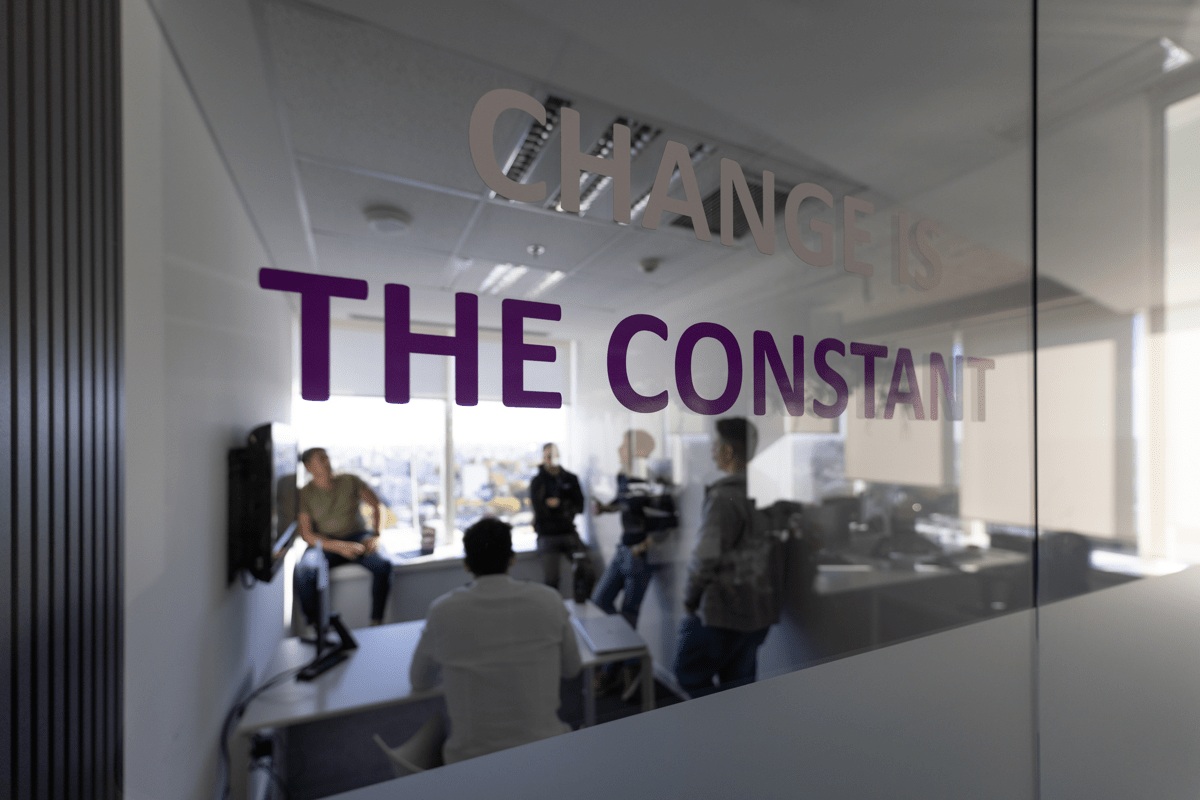 People meeting behind an office glass wall bearing the words Change is the constant