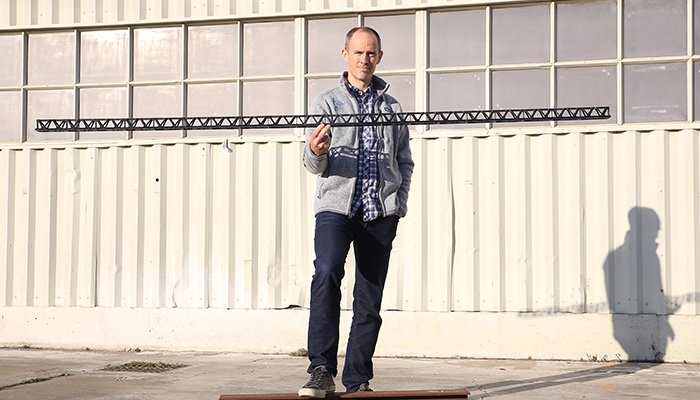 Ethan Escowitz standing outside ARRIS holding a long carbon-fiber truss