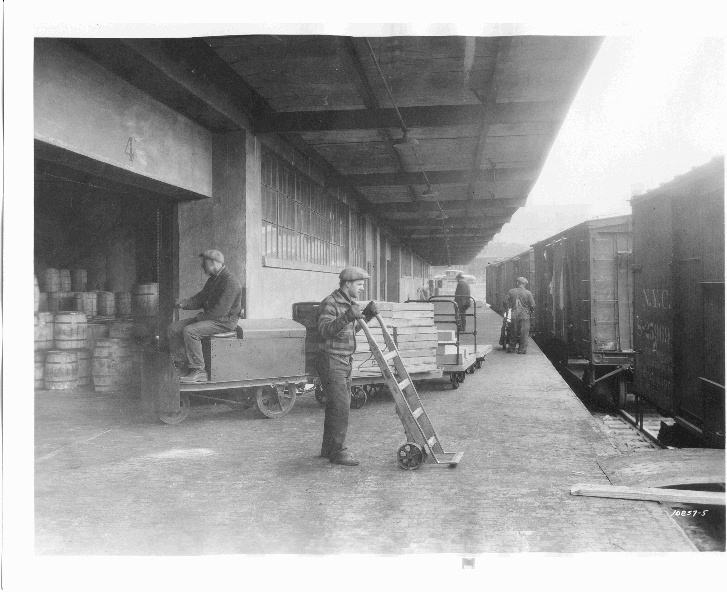 Evans warehouse workers using hand trucks beside rail cars in 1929
