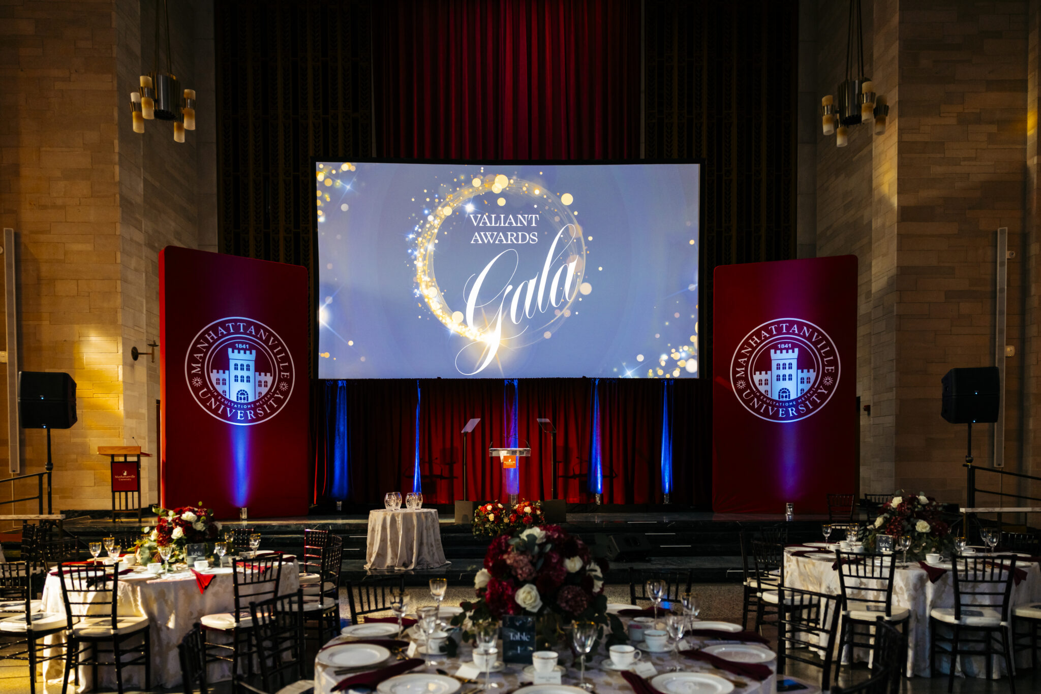 A formal Valiant Awards gala produced in a grand hall, with a lit stage, banquet tables and floral centerpieces
