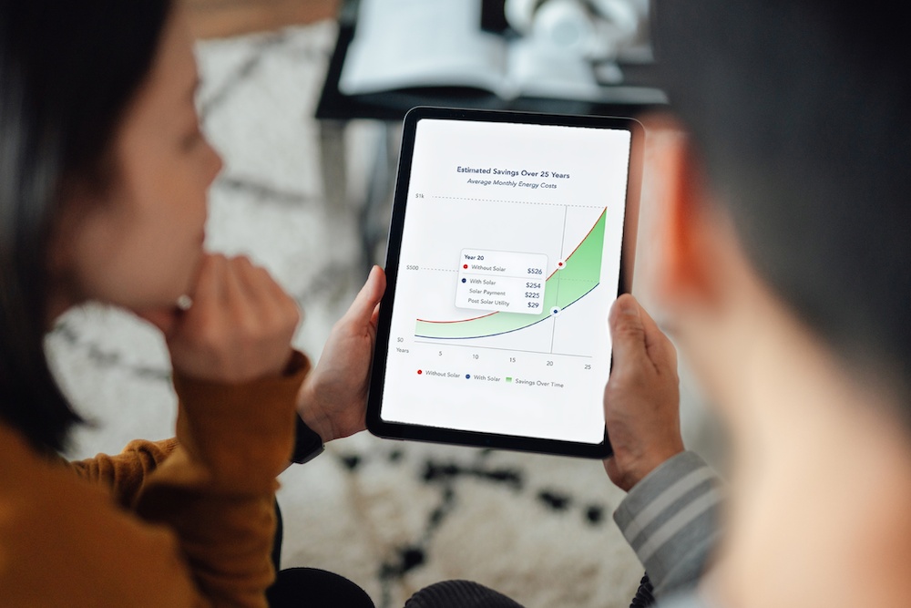 EverBright marketing photograph of a couple reviewing a 25-year energy-cost projection on a tablet