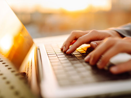 Hands typing on a laptop at a desk in warm evening light