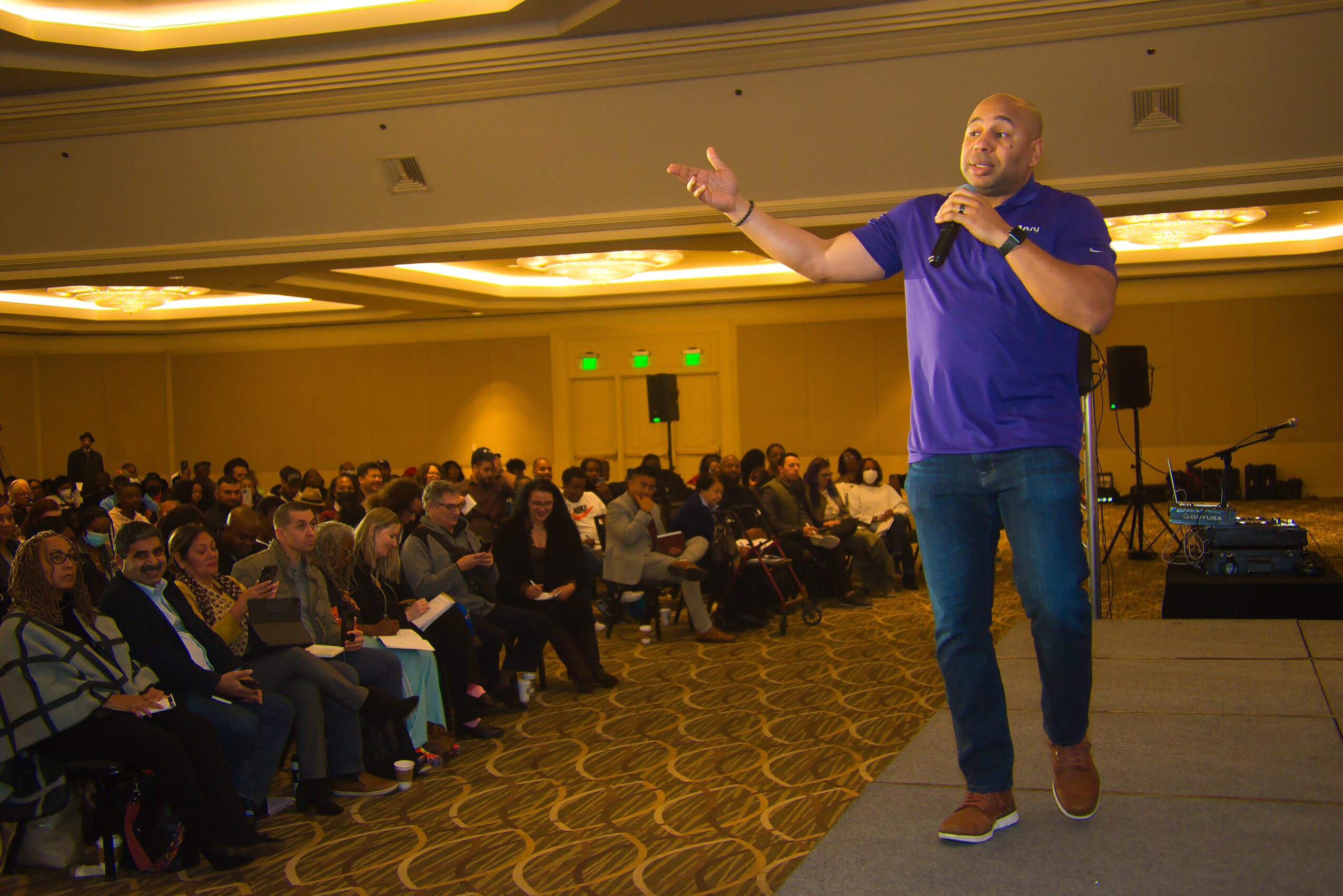 Everett Sands holding a microphone and addressing a seated audience