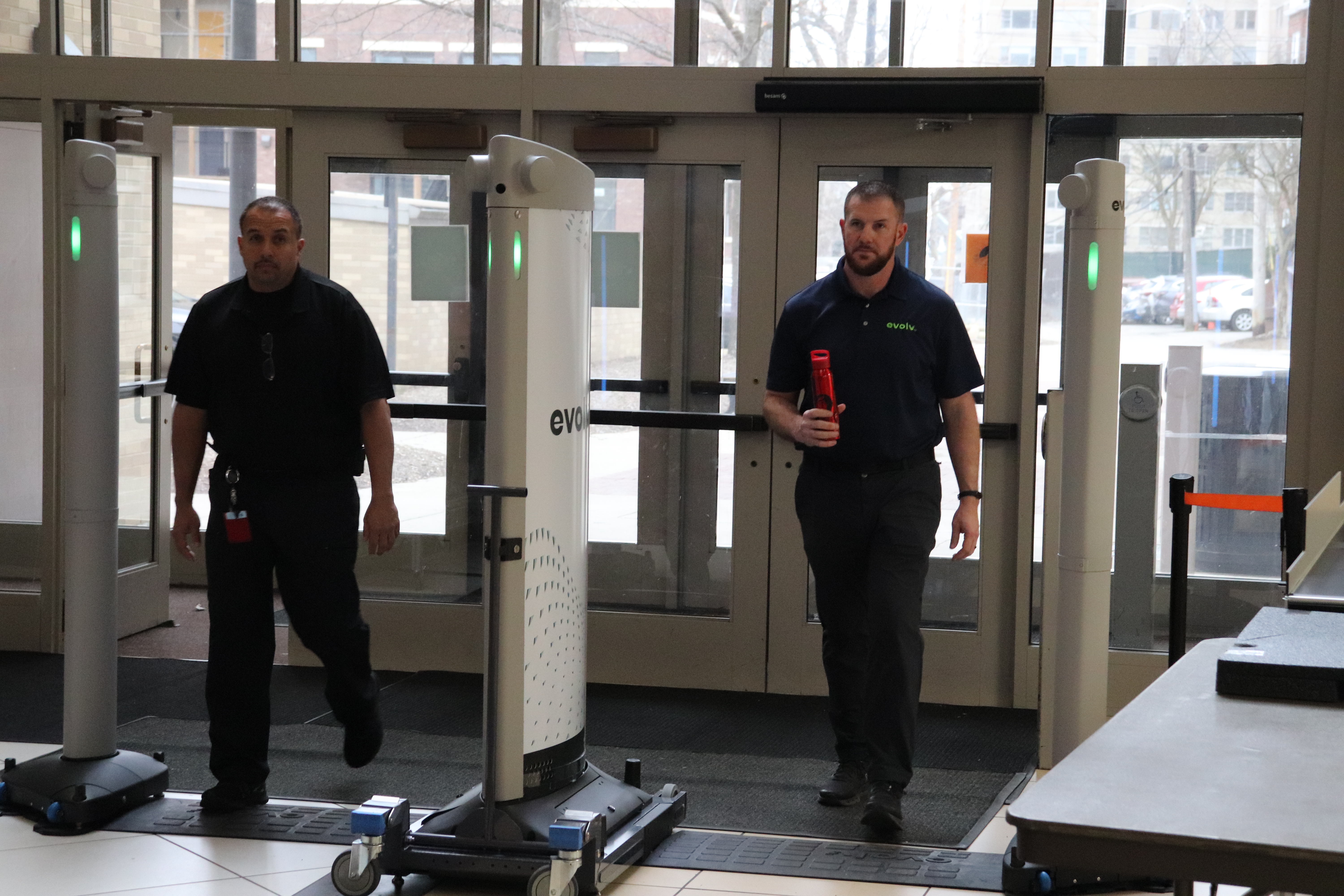 Two staff members demonstrate an Evolv Express screening lane in a school lobby