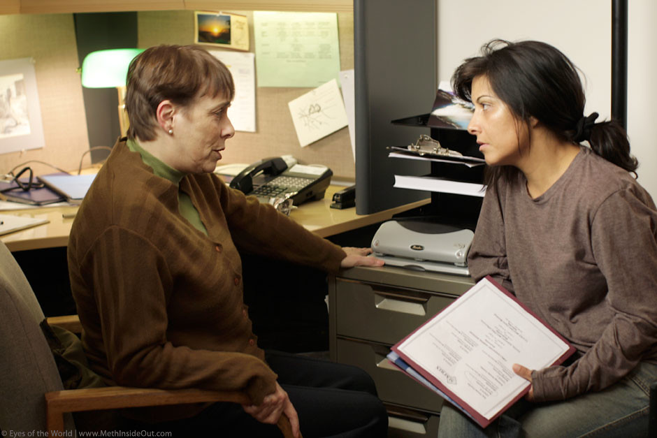 Two women seated beside an office desk, one holding an open folder, in the company’s Meth-Individual-Attention photograph.