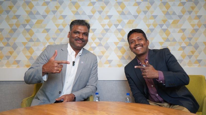 Ezhilarasan Natarajan, left, and Karthik Chidambaram smiling and pointing toward each other during a podcast recording.