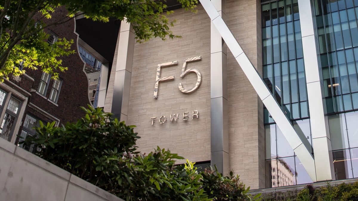 The F5 Tower entrance in Seattle, framed by trees and the building’s glass facade