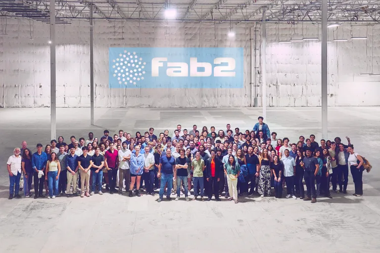 Fab2 employees gathered in an industrial building beneath a company banner