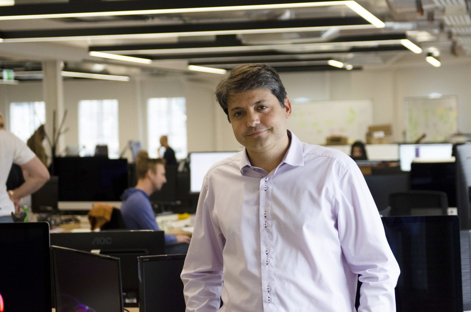 Fabio Kuhn standing among desks and computer screens in a Vortexa office
