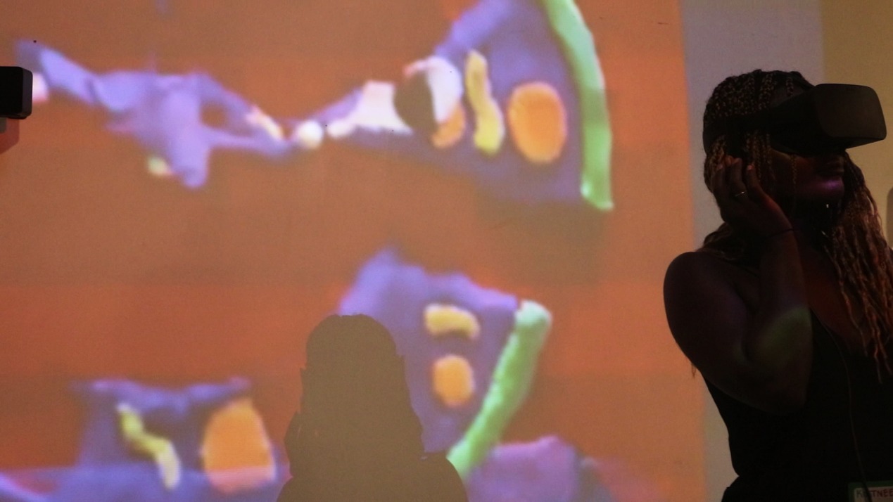 A visitor wearing a virtual-reality headset inside Fabric Studios, silhouetted against a colorful projected image