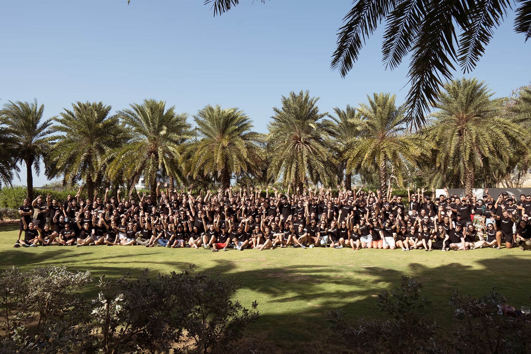 A large group of Factored team members gathered outdoors beneath palm trees