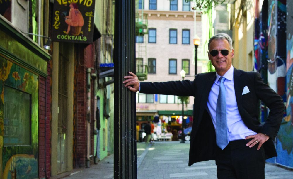 Fahri Diner in a suit and sunglasses, standing in a city alley
