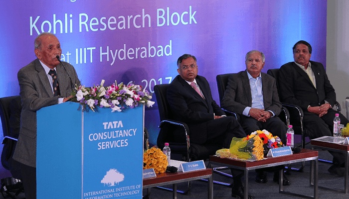 F C Kohli speaking at a lectern at IIIT Hyderabad, with other participants seated beside him