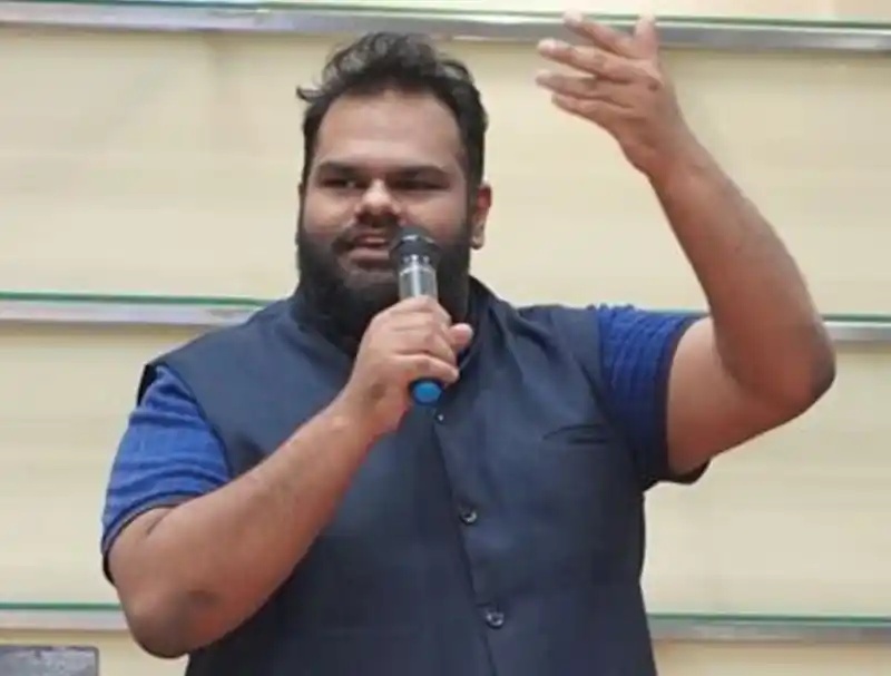Faraz Moosa speaking into a microphone with one hand raised