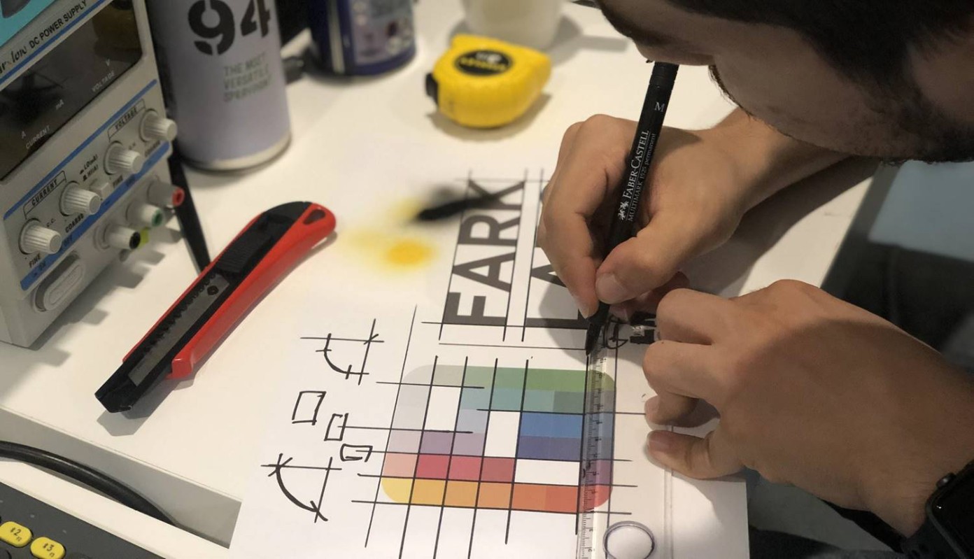 A designer draws a measured grid over a colorful Fark Labs graphic