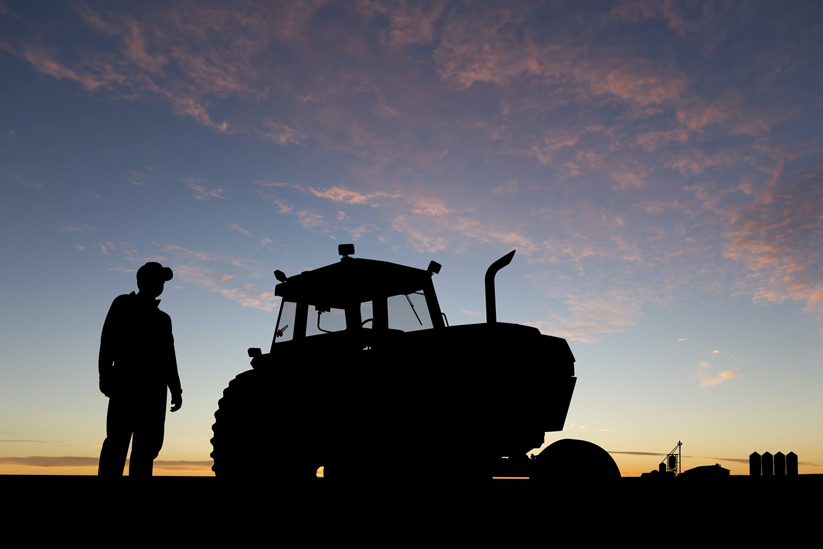 A farmer and tractor silhouetted against a colorful evening sky in a Farm Journal Studios image