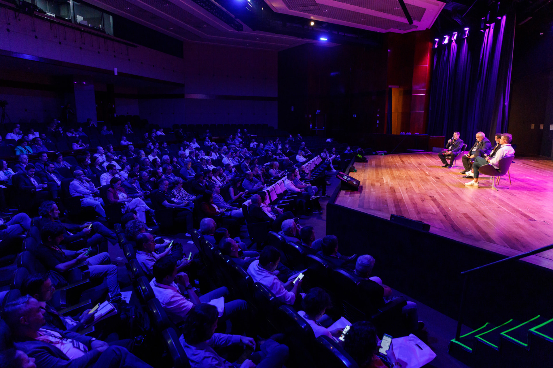 A packed audience facing the brightly lit stage at an FCJ innovation summit