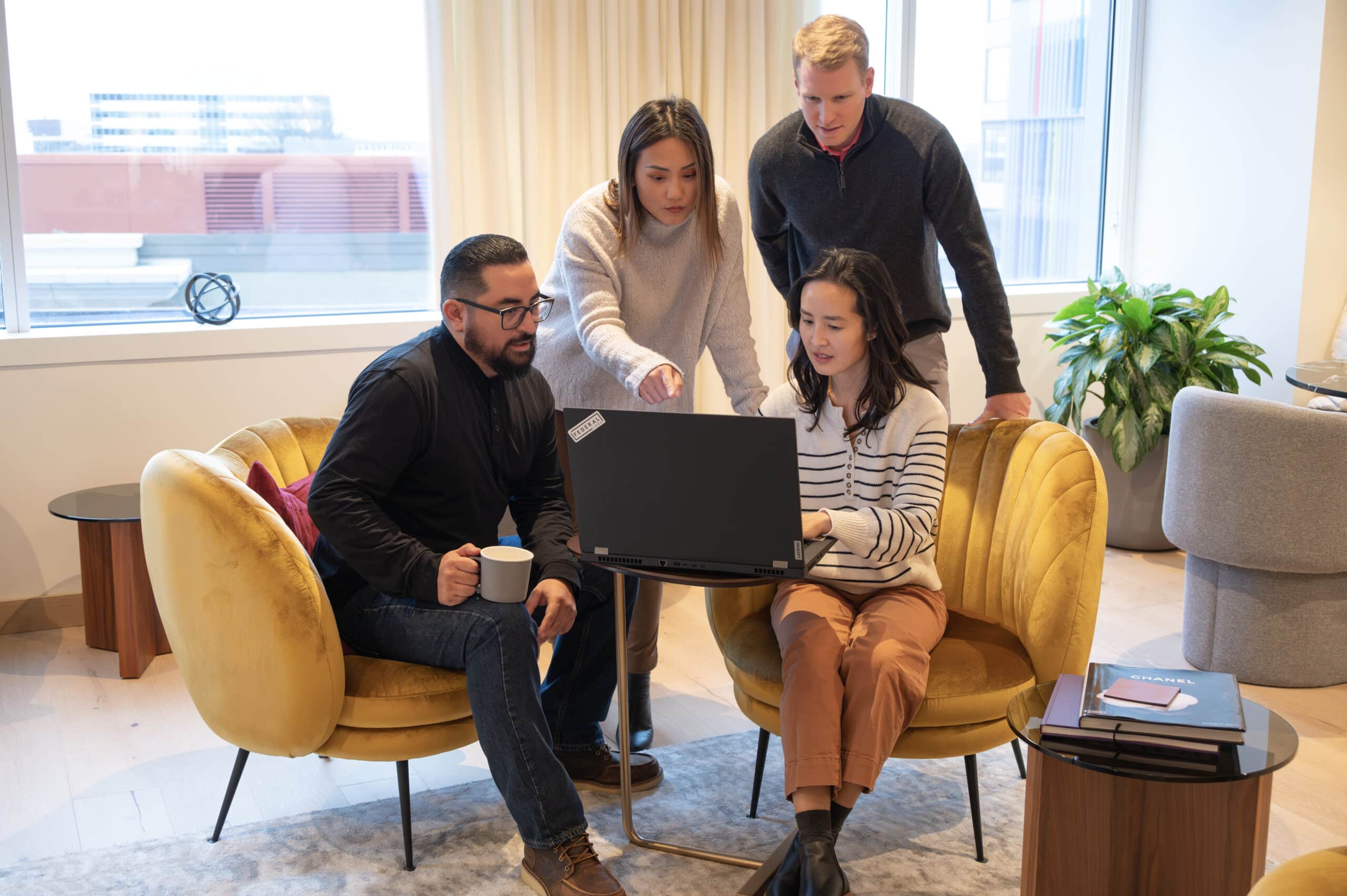Four Federal Realty colleagues gather around a computer in an office seating area