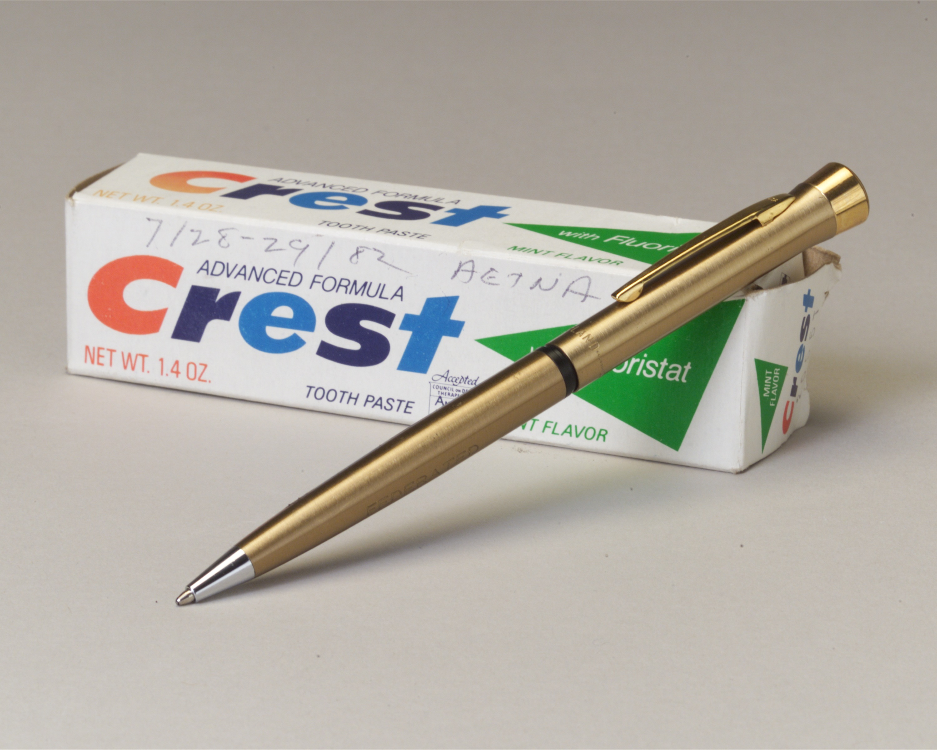 A Crest toothpaste box marked with the July 1982 Aetna negotiation dates, beside a gold-colored pen