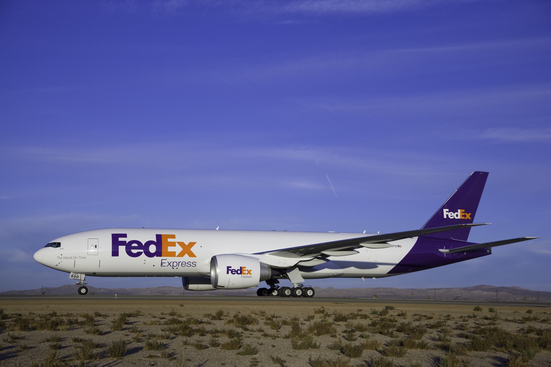 A FedEx Boeing 777 freighter on an airport taxiway beneath a blue sky