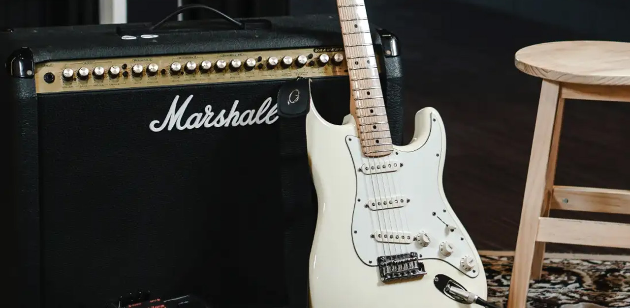 An electric guitar leans against a Marshall amplifier beside a wooden stool