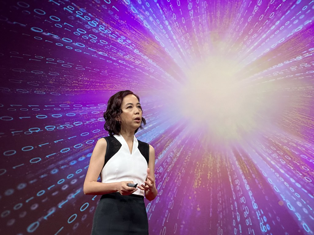 Fei-Fei Li speaking onstage at TED 2024 beneath a projected field of digits