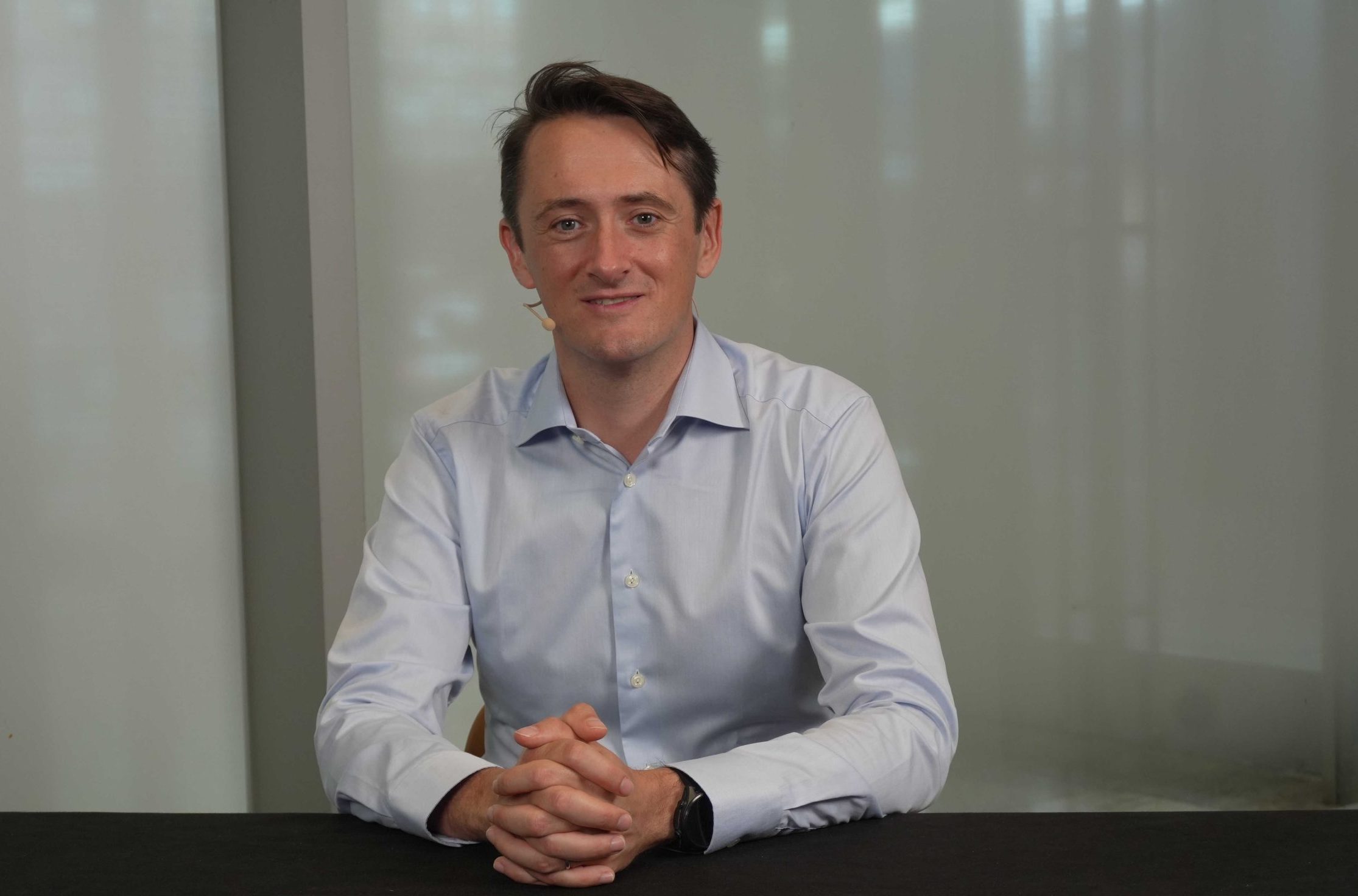 Felix Van de Maele seated for an interview, wearing a headset microphone and a light blue shirt.