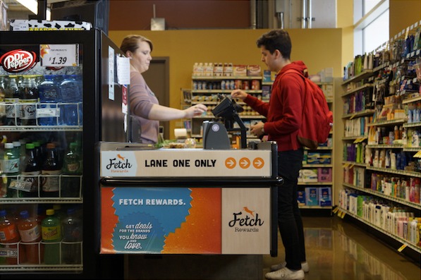 A shopper demonstrates Fetch's original in-store checkout product at Fresh Madison Market while a cashier looks on.