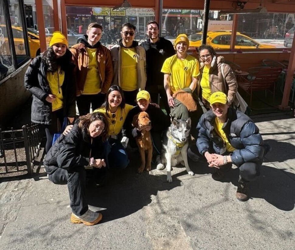 Fi team members in yellow clothing posing outdoors with dogs
