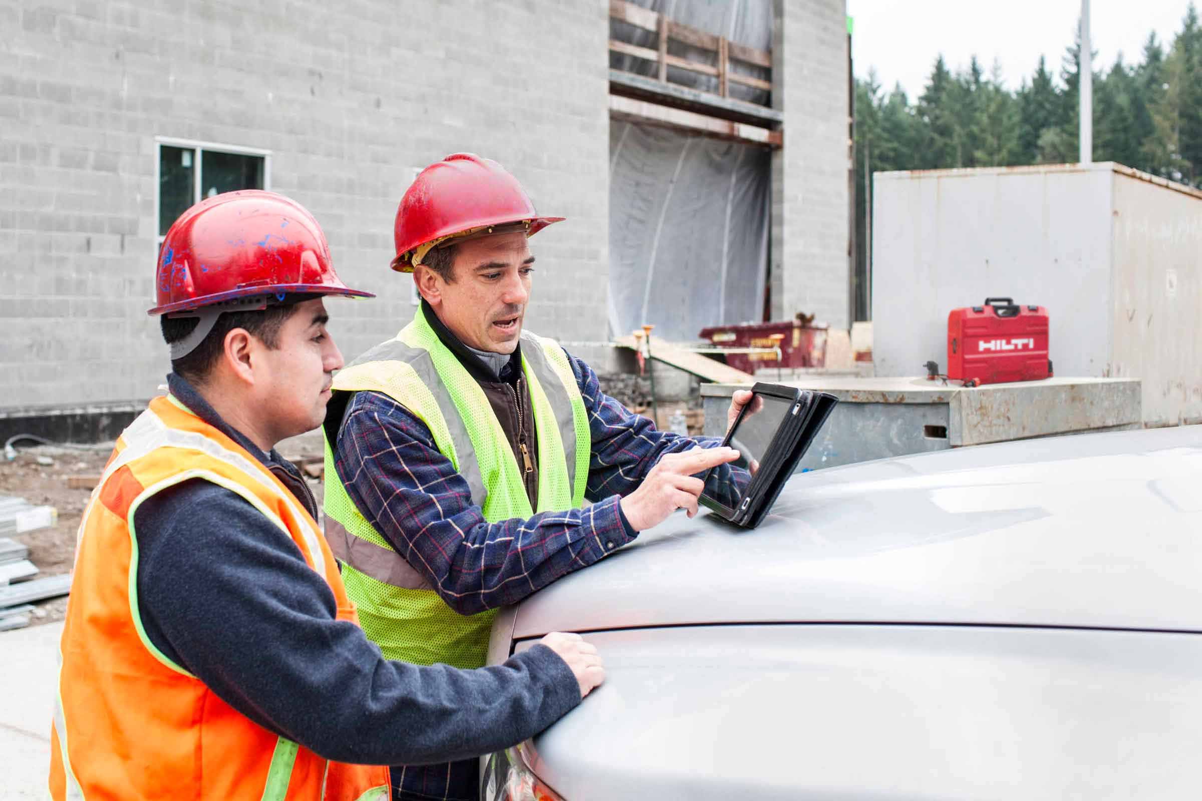 Two construction workers reviewing a tablet beside a Hilti toolbox