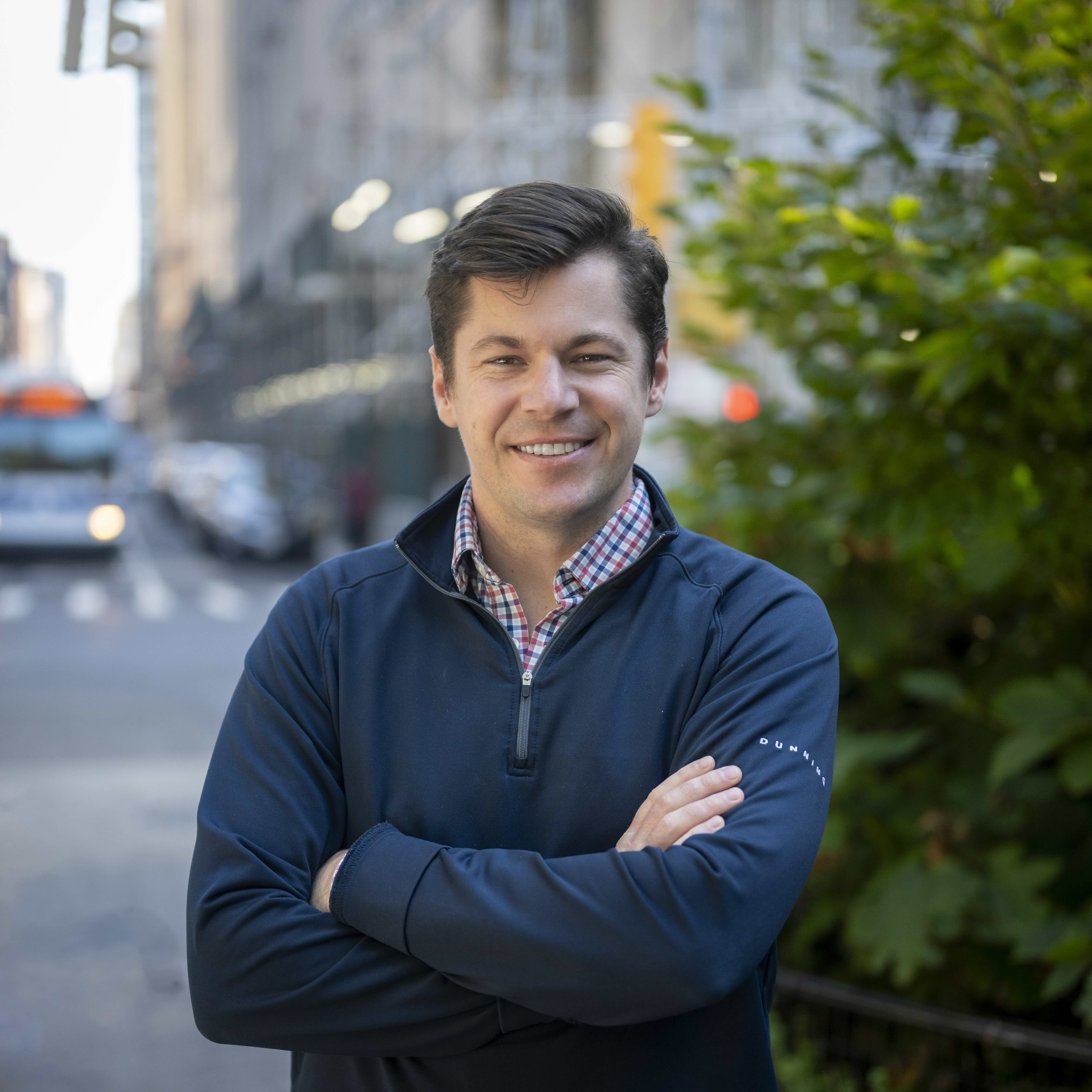 A Finch co-founder on a New York City street, arms crossed, with the city's morning traffic behind him