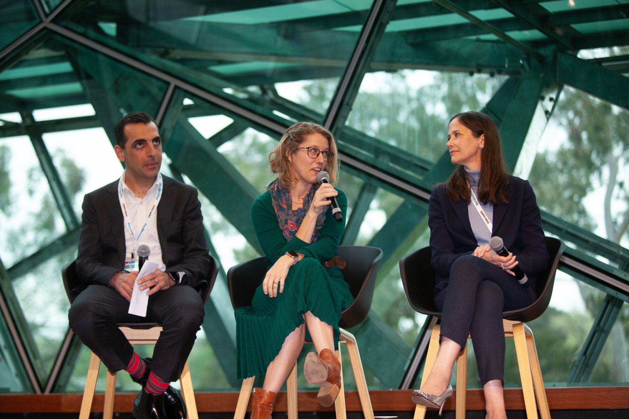 Three seated participants in a fintech panel discussion, with a speaker holding a microphone.