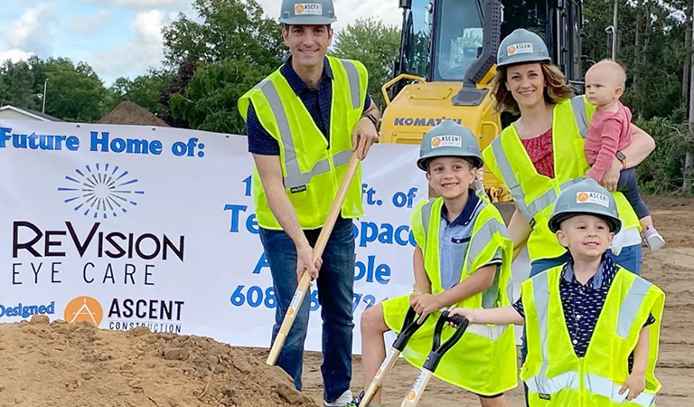 Family in hard hats and safety vests at a groundbreaking beside a ReVision Eye Care sign