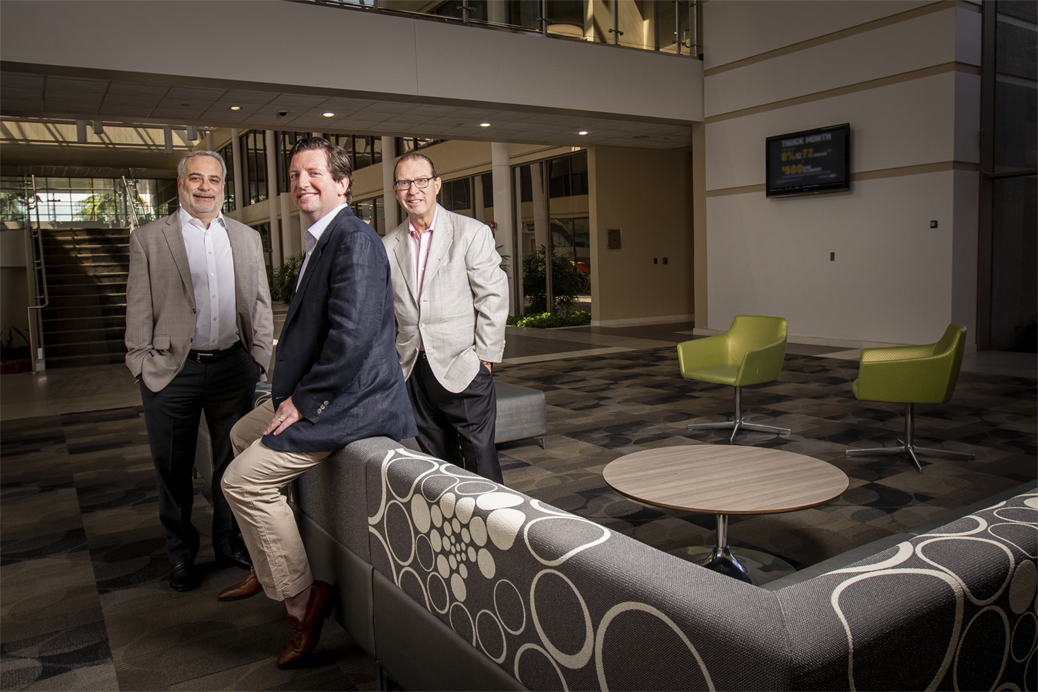 Three FlexShopper executives posing beside a patterned sofa in a spacious office atrium in 2020