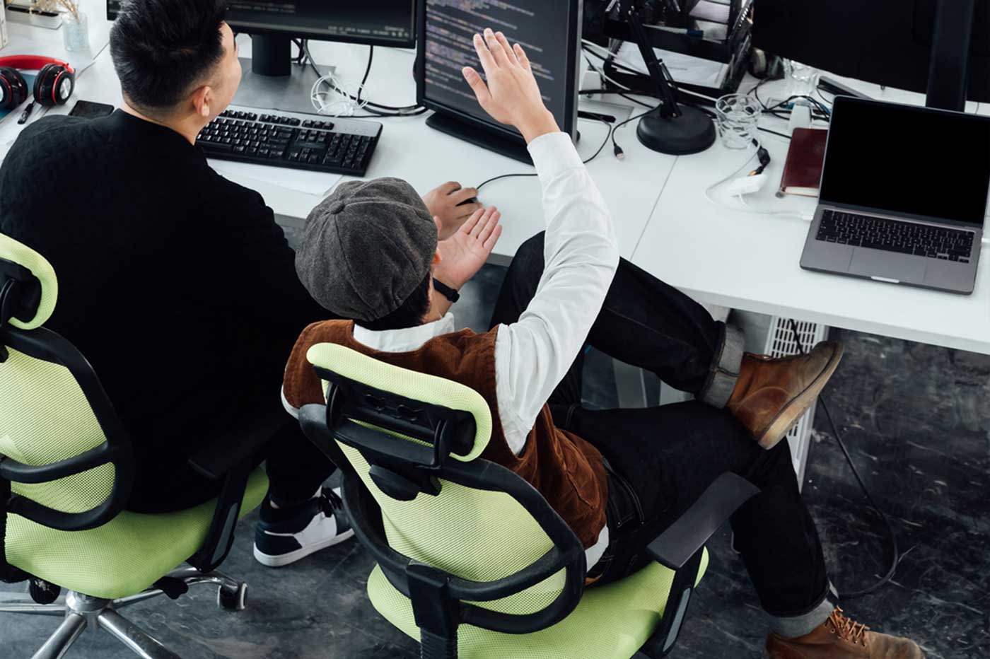 Two people discussing code across several monitors in a workplace