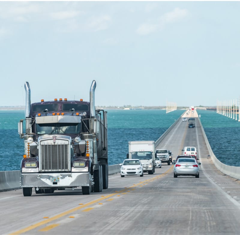 A semi-truck and other vehicles travelling across a bridge over water