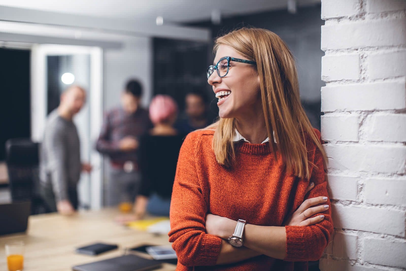A woman in an orange sweater smiles in an office scene used on Flooid’s careers pages.
