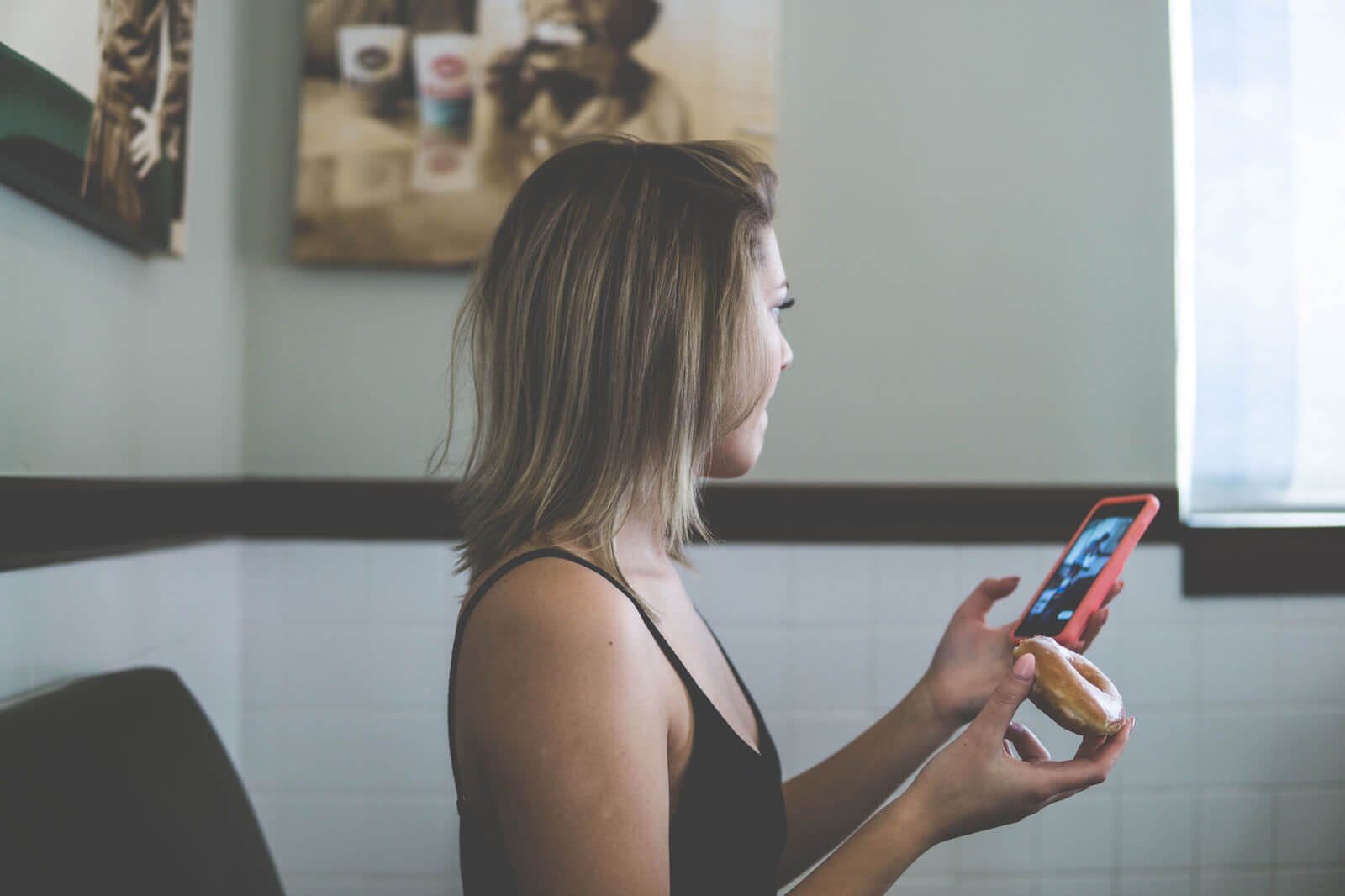 A customer holds a doughnut and checks her phone in an image from Flooid’s Krispy Kreme case study.